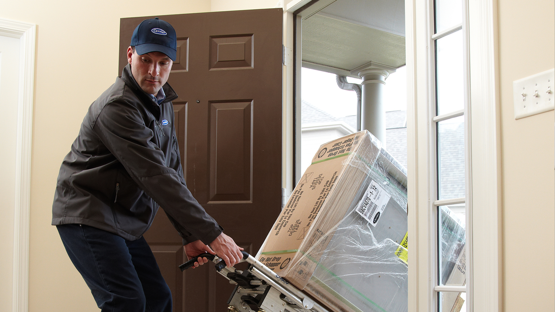 Carrier dealer rolling a gas furnace through the front door of a home
