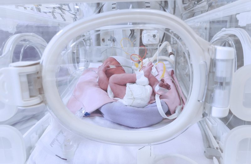 Newborn baby girl inside incubator in hospital post delivery room