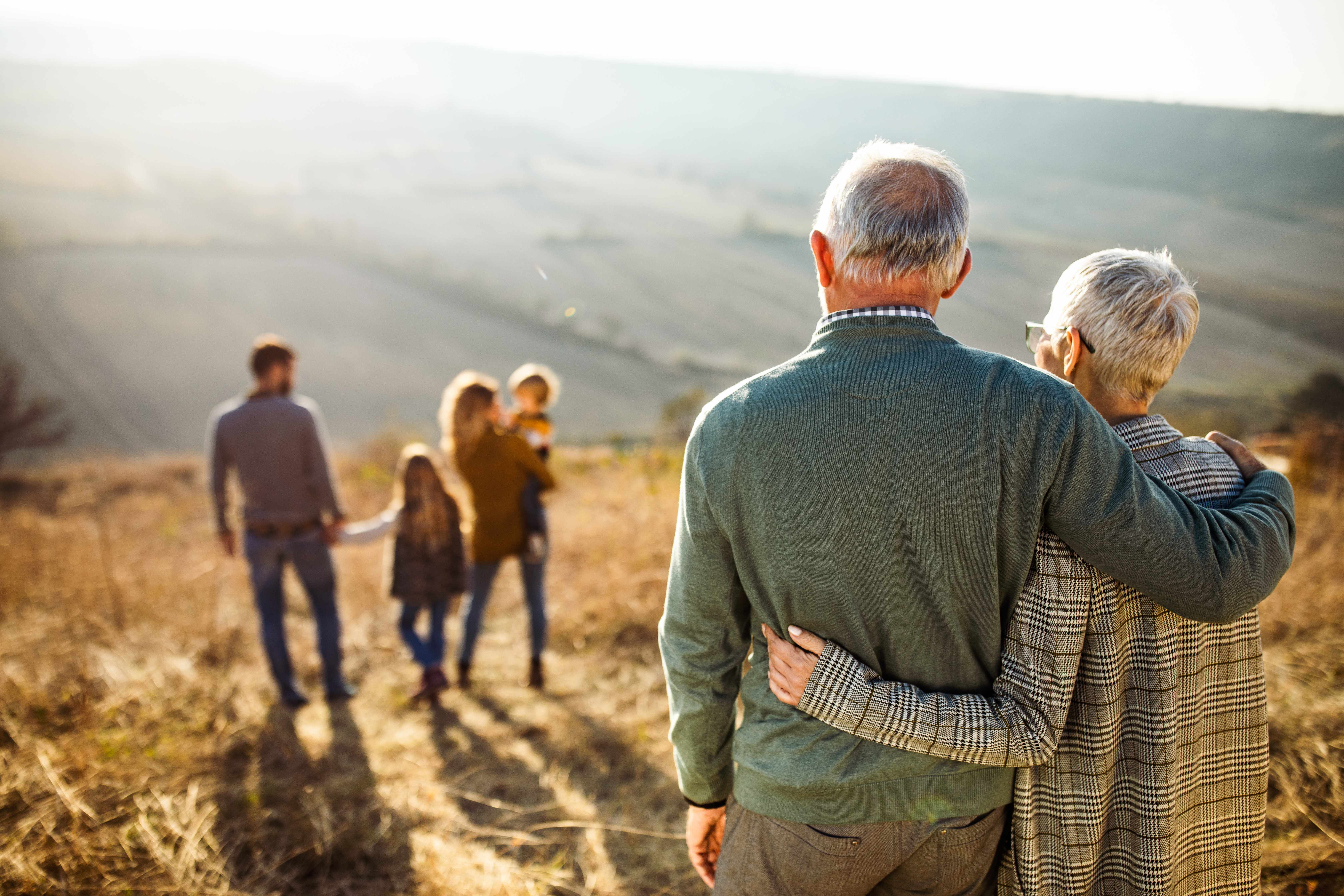 Back view of grandparents looking at their family on a field in autumn day.