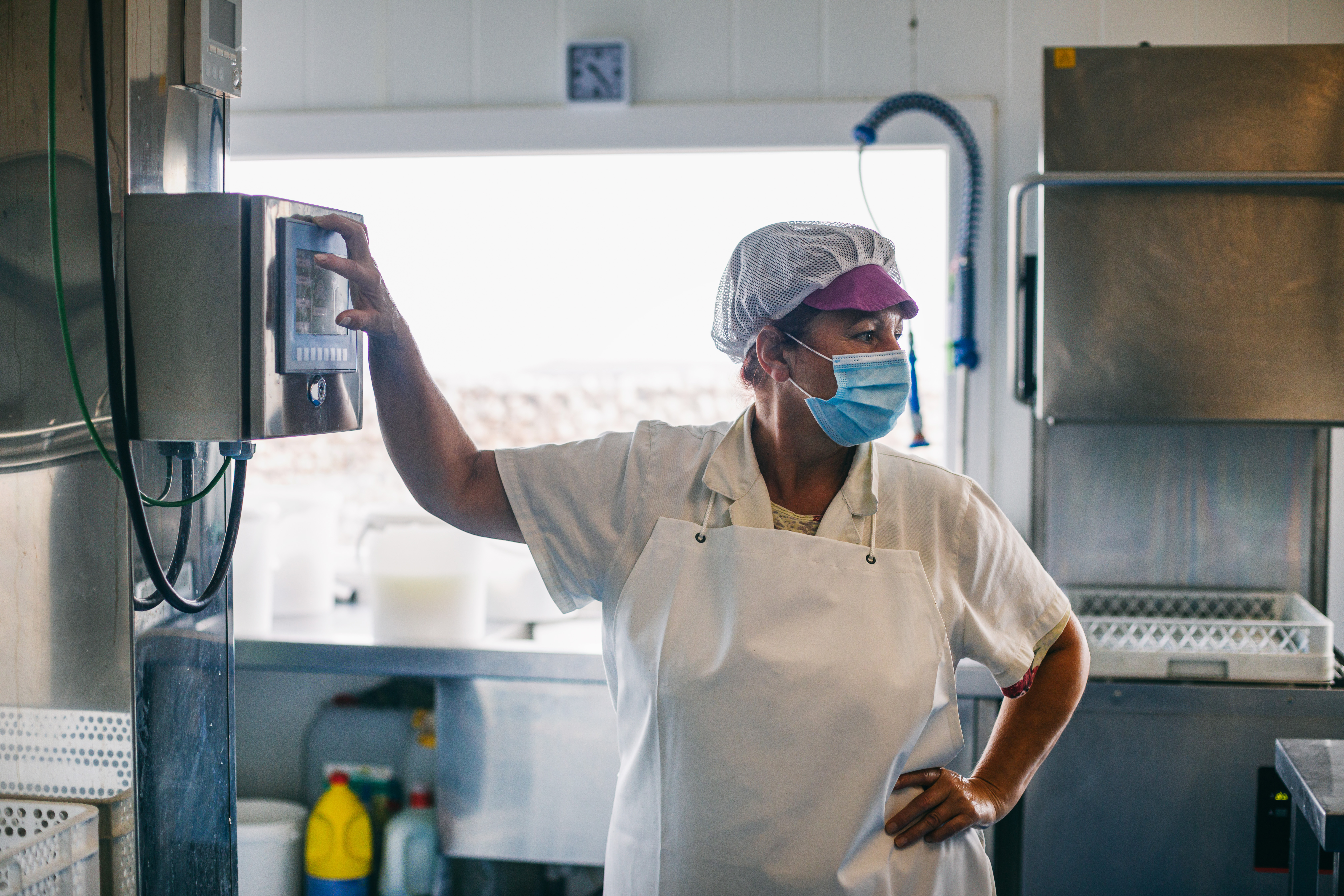Female worker in uniform and mask pressing button on control panel.