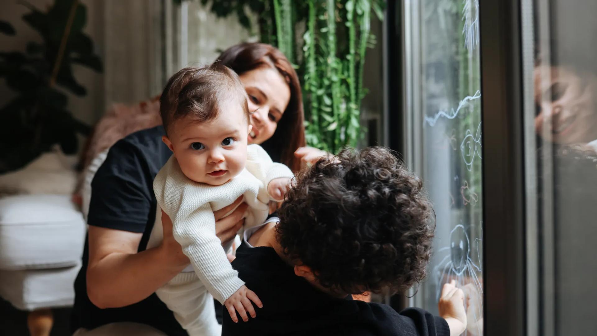 Young kids are hugging their mother in their home.