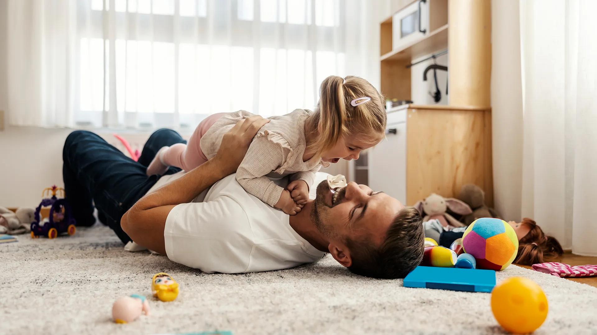 A father and young daughter laughing and playing on the floor while enjoying their indoor air quality systems