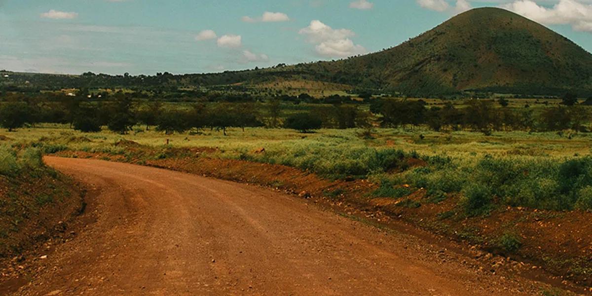 Dirt road in Africa with green hills and mountain in background