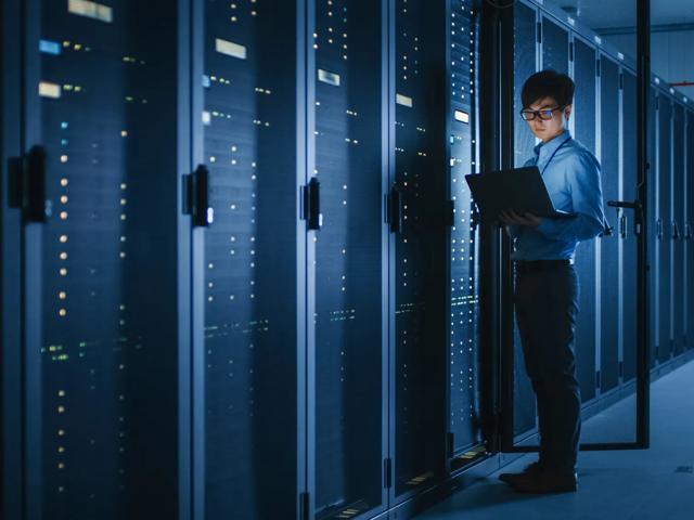 man in data center server room with laptop