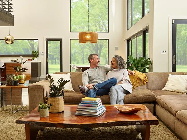 A man and woman sitting on a couch talking about their new 33NM3 domestic hot water air-to-water heat pump