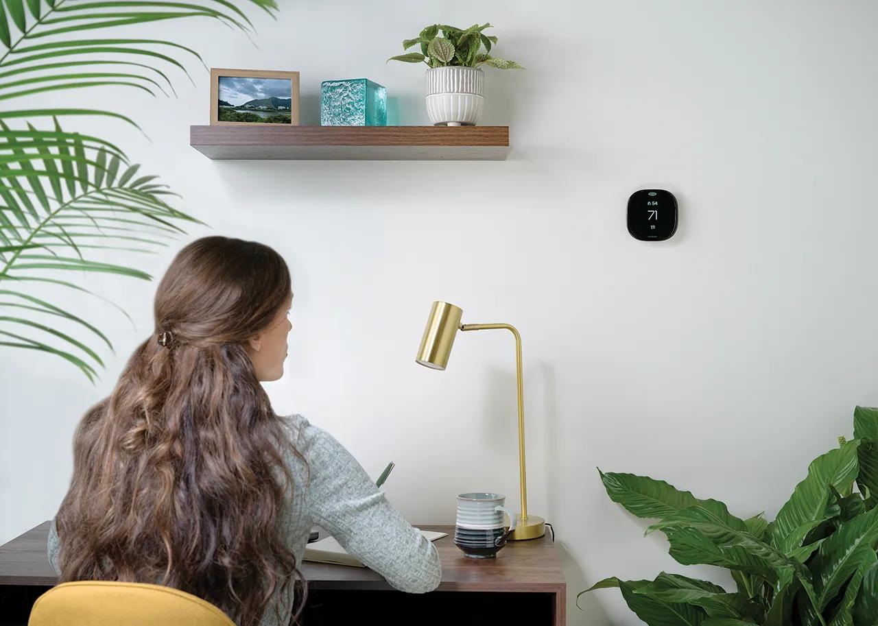 woman sits at desk by ecobee thermostat