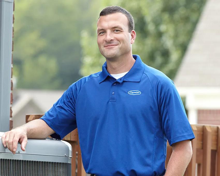 A Carrier dealer smiling standing next to an AC unit