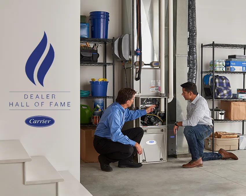 A Carrier dealer showing a man a furnace with the Carrier dealer hall of fame logo nearby
