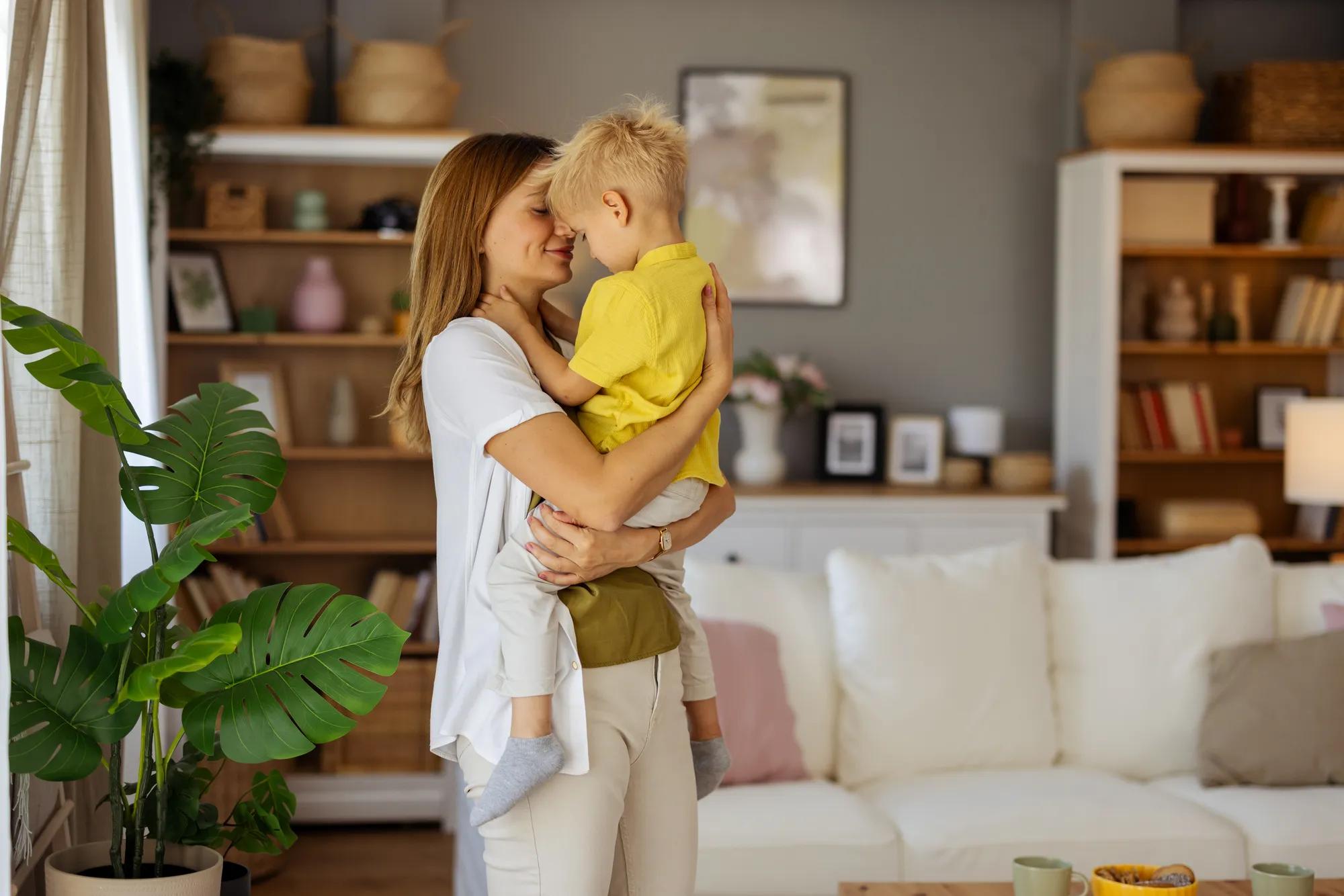 Mother holding boy while standing in living room.